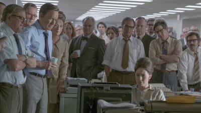 Redaktionen på Washington Post står alla samlade kring ett bord och tittar på tv-nyheterna.