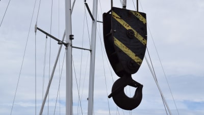 En krok till en lyftkran hänger framför några segelbåtsmaster.