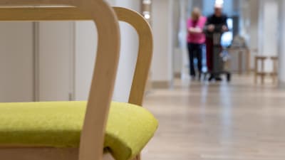 Fysioterapeutti avustaa vanhusta kävelyharjoituksessa Myyrmäen vanhustenkeskuksessa. Etualalla kuvassa tuoli.