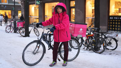 Bild på Anton Salmenkylä i rosa jacka och hans cykel med en rosa termobox bakpå.