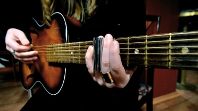 Närbild på en gammal akustisk gitarr som spelas med ett sliderör.
