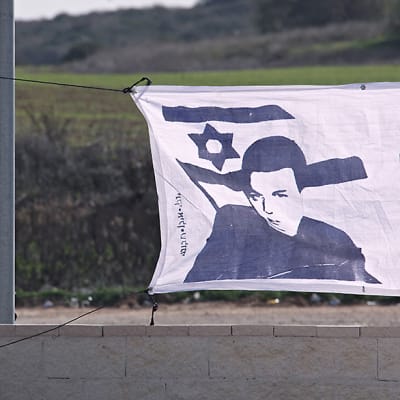 Palestiinalaisnainen kävelee kärrynsä kanssa Shalitia esittävän julisteen ohi.