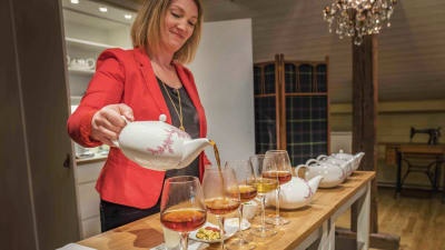 Nainen punaisessa jakussa kaataa teekannusta teetä viinilasiin