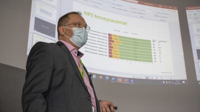 Ilkka Pirskanen håller en presentation. Power point med staplar i bakgrunden.