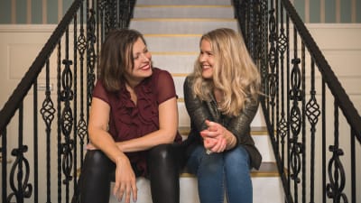 Eva Frantz och Hannah Norrena sitter i en trappa och skrattar.