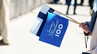 Finlands flagga och Finland 100 flagga i en medborgares hand, 2017