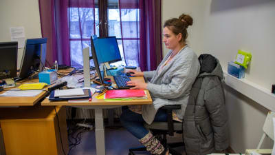 En kvinna sitter vid ett skrivbord och skriver på tangentbordet till en dator.