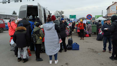 En folksamling, mest kvinnor och barn bakom och bredvid en buss.
