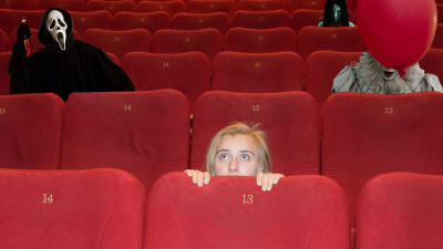 En ung kvinna kryper ihop bakom biografstolen, bakom henne syns olika monster från skräckfilmer.