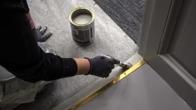 En hand med en pensel som målar ett golv.