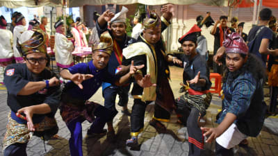 En grupp festklädda malaysiska män tittar mot kameran och intar olika kampställningar.