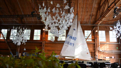 En stor festsal med en segelbåt med hissade segel. I taket hänger konstverk som ser ut som mängder av små segelbåtar.
