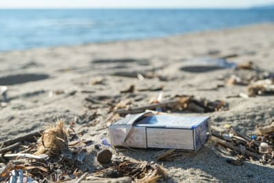 En tobaksask och annat skräp ligger på en strand.
