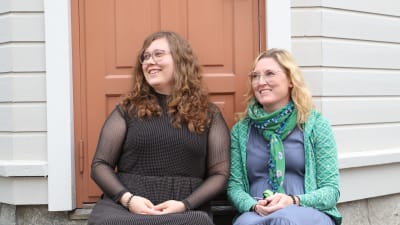 Två kvinnor tittar åt sidan och ler.