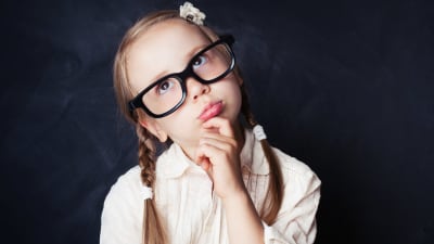 En flicka med flätor och glasögon står och funderar på något.