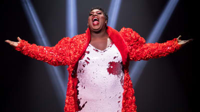 Latrice Royale iklädd en rödvit glittrig klänning står med utbredda armar och sjunger.  