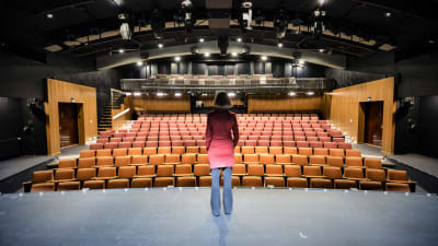 Kvinna i brun page ser ut över en tom teatersalong.