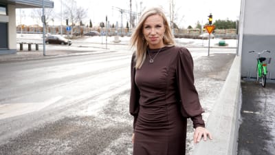Kvinna i mörkbrun klänning står på en trottoar.