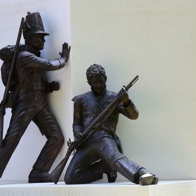 Brittisotilas punaisessa univormussa ja karvalakissa vartioi patsasta, joka esittää kahta 1800-luvun sotilasta.