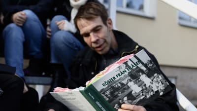Man sitter med en kaffekopp i handen och läsen ur en bok.