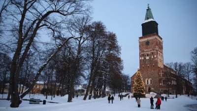 Människor framför Åbo domkyrka och domkyrkans julgran i ett vintrigt landskap.