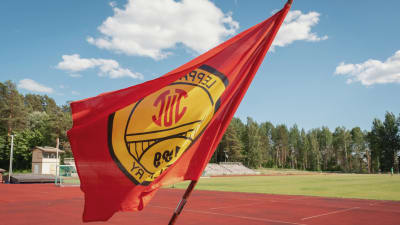 Punakeltainen lippu liehuu kesällä urheilukentän edessä.