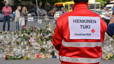 Person med röda korsets väst vid gravljus på Åbo torg.