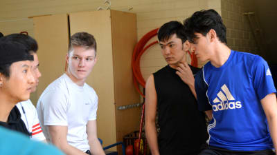 Fem afghanska och en finsk spelare pratar på bytesbänken i ett rum för idrottsredskap.