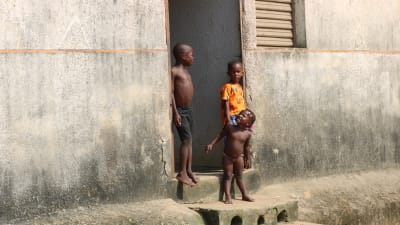Tre barn står i en dörröppning till ett betonghus i Abobo, Elfenbenskusten.