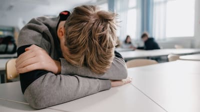 En elev lutar sitt huvud mot ett bord i ett klassrum.