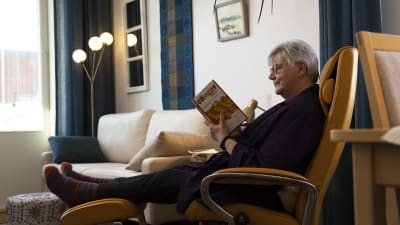Tiina Henkola lukee kirjaa "Comedy Bible" ja istuu nojatuolissa.