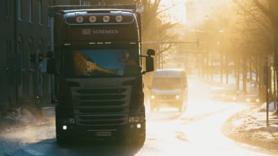 En långtradare kommer körandes i motsljus längsmed en blöt och snöig gata i Helsingfors. 