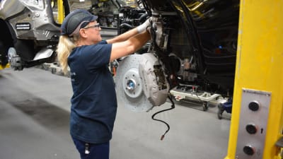 Galina Koskelainen, en dam med blont hår i hästsvans under en blå skyddsmössa, monterar delar på en bil i en bilfabrik.