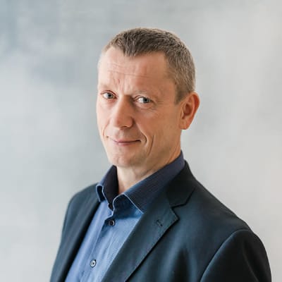 Mies sininen kauluspaita ja pikkutakki päällä poseeraa kameralle.