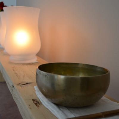 Äänimalja, kynttilöitä ja kukkia hyllyllä.