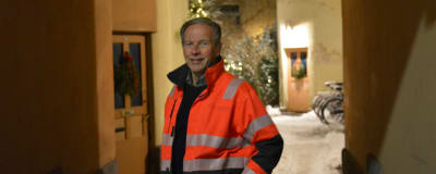 Ben Mattsson i orange kläder står i en portgång med en julgran i bakgrunden.