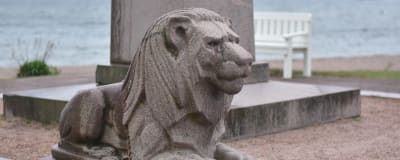 En lejonstaty som är en del av ett monument i sten. Hav i bakgrunden. 
