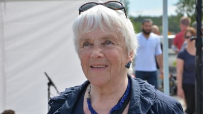äldre dam med vitt grått hår och solglasögon står under ett tält på de vita pärons potatisfestival i nagu.