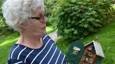 elisabeth westerholm står i trädgården och håller ett tittskåp i händerna. Skåpet är en miniatyrmodell av ett redskapsskåp för en trädgård. 