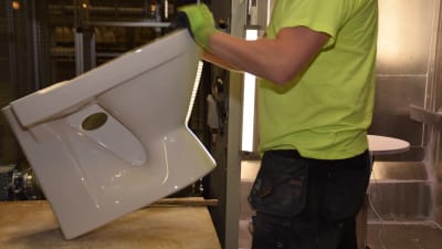 En arbetare på Ido badrums fabrik i Ekenäs granskar med sina händer att wc-stolen är hel.