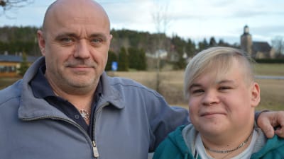 Far och son poserar utomhus med Kimito kyrka i bakgrunden.