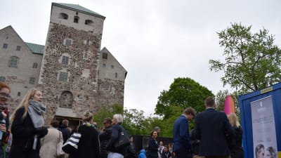 Människor minglar framför försäljningsstånd under businessfestivalen The Shift, Åbo slott i bakgrunden.