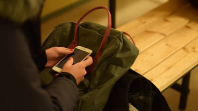 person med mobiltelefon och ryggsäck i knät