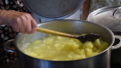 En hand håller i en slev och rör om i en stor kastrull med potatis.