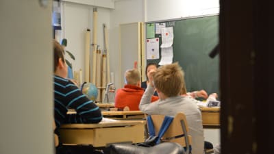 Barn sitter med ryggarna åt kameran i ett klassrum