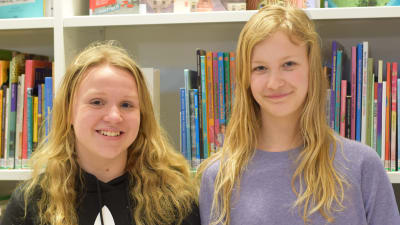 Två unga flickor framför en bokhylla med barnböcker