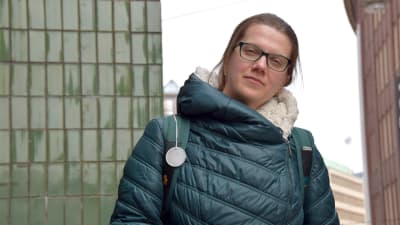 Maria Eliseeva iklädd mörkgrön täckjacka står och tittar rakt in i kameran med några stora våningshus i bakgrunden.