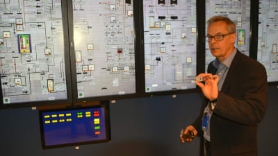 Ulf Lindén håller upp en analog brytare framför en pekskärm i Lovisa kärnkraftverks simulator.