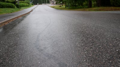 En väg som är våt av regn. I asfalten syns märken efter att en moped har bromsat.