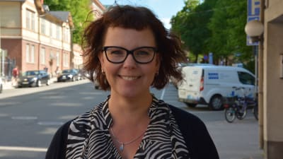 Kvinna med rödbrunt hår och glasögon står leende på Trädgårdsgatan i Åbo.
